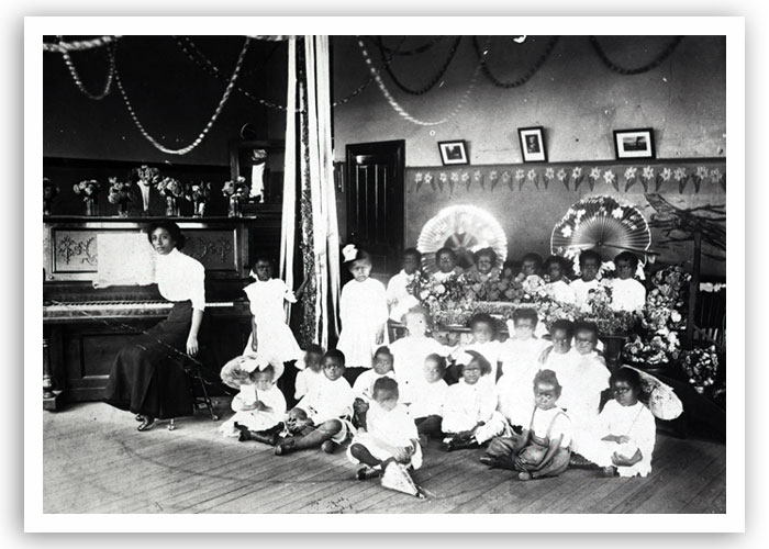 Group of children and their teacher in music class in Guthrie, date unknown. The photo possibly highlights some kind of pageant.