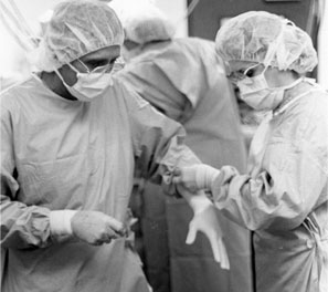 A nurse helps Dr. Nazih Zuhdi into surgical gloves before the first heart transplant in Oklahoma