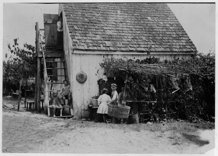 Name: Three families is the rule in these shacks, one room above and one below, but sometimes four families crowd in. Outdoor dining room at side[?] Maryland. 1909 July. (Lewis Hine/Photo courtesy of LOC)