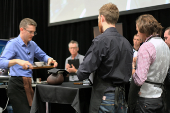 Ben Bicknell stands at the judges table with Peter Wolfe while runner-up champion, Simon James, presents his signature drinks at the 2010 Australian Barista Championships.