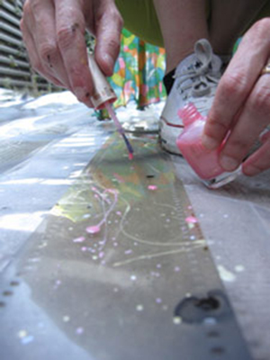 Jennifer West applying nail polish to film strips for <em>Lavender Mist Film/Pollock Film 1 (70mm film leader rubbed with Jimson Weed Trumpet flowers, spraypainted, dripped and splattered with nail polish, sprayed with lavender mist air freshener)</em>, 2009. 46 sec. Photo: Finn West. Jennifer West applying nail polish to film strips for <em>Lavender Mist Film/Pollock Film 1 (70mm film leader rubbed with Jimson Weed Trumpet flowers, spraypainted, dripped and splattered with nail polish, sprayed with lavender mist air freshener)</em>, 2009. 46 sec. Photo: Finn West.