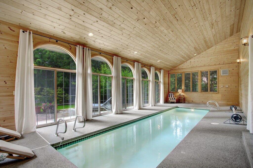 Sloped wood ceiling indoor in-ground swimming pool with one wall lined with floor-to-ceiling arched windows. Sloped wood ceiling indoor in-ground swimming pool with one wall lined with floor-to-ceiling arched windows.