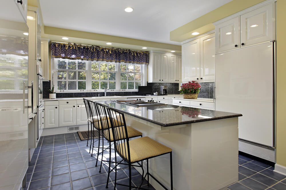 This kitchen uses extensive white in contrast with dark blue tile flooring and window dressing, with light yellow wall accent color. This kitchen uses extensive white in contrast with dark blue tile flooring and window dressing, with light yellow wall accent color.