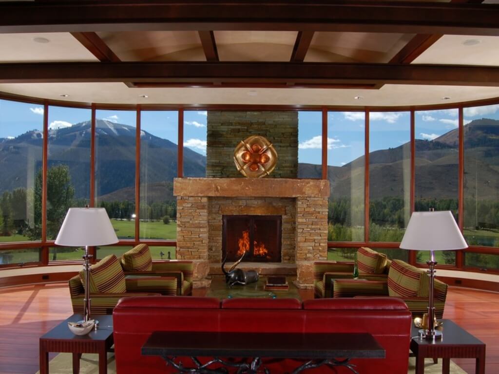 Luxurious living room with brick fireplace and huge bay window overlooking the golf course. The living room is decorated with one red leather sofa flanked by 2 side tables Luxurious living room with brick fireplace and huge bay window overlooking the golf course. The living room is decorated with one red leather sofa flanked by 2 side tables