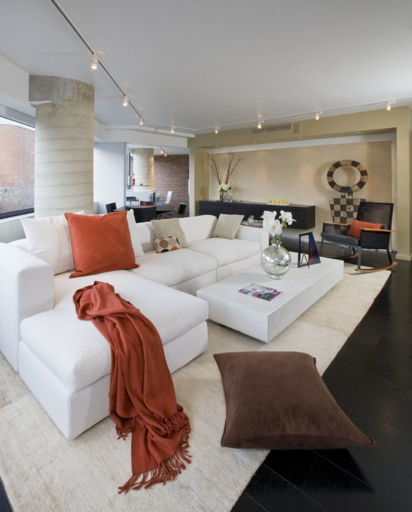 Living room centers furniture on light area rug around "floating" coffee table in matching white. Embedded lighting in far wall highlights art pieces and similarly "floating" black wall-mounted cabinetry. Living room centers furniture on light area rug around "floating" coffee table in matching white. Embedded lighting in far wall highlights art pieces and similarly "floating" black wall-mounted cabinetry.