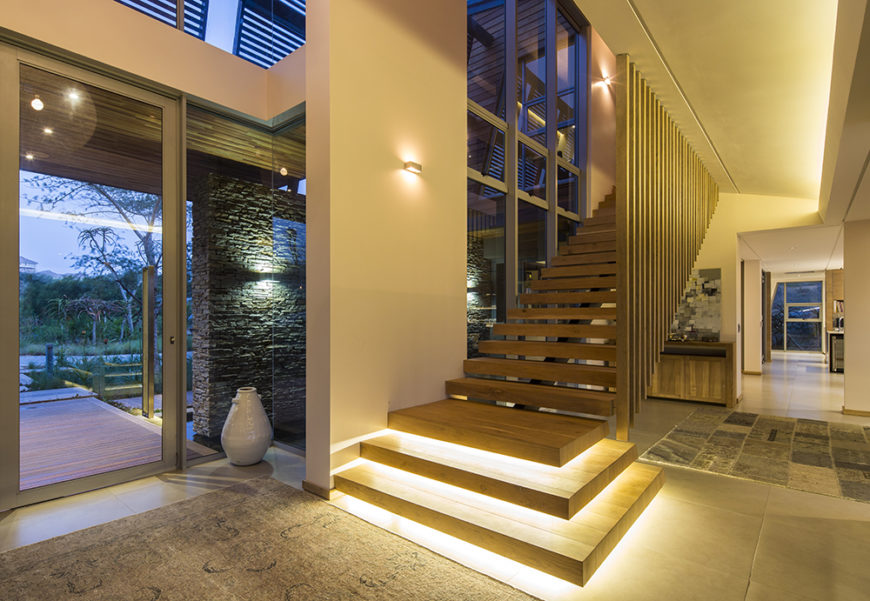 Here at the main entry to th ehome, we see open design staircase leading toward the bedroom areas, with built-in lighting beneath the steps. The front entry is all steel and glass, framed in stone.
