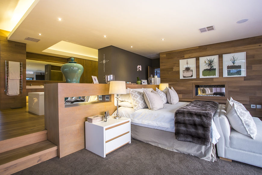 The master bedroom is a luxurious suite, combining several major elements over a layered floor plan. The bed area sits lowest, near sliding glass doors that access the balcony, while an en suite bathroom sits on a raised wood area.