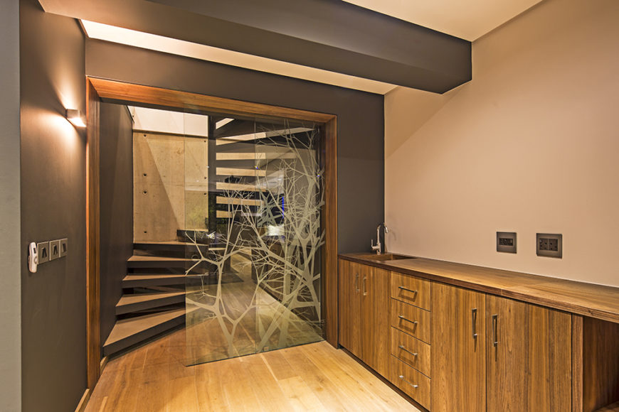 Moving to the lower level of the house, we see more hardwood flooring, natural wood cabinetry, and an intriguing glass divider wall with laser etched tree designs.