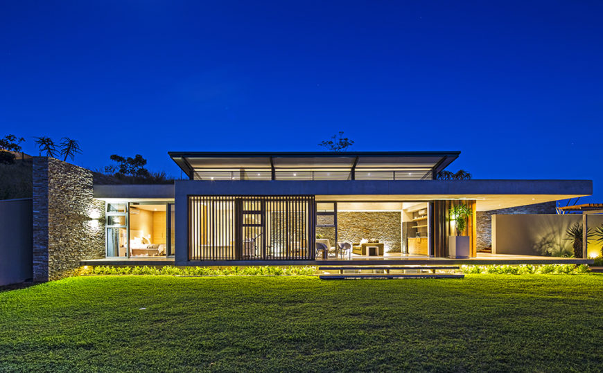 Seen from across the back lawn, the home positively glows from within. We can see right through to the interior, courtesy of those massive glass panels.