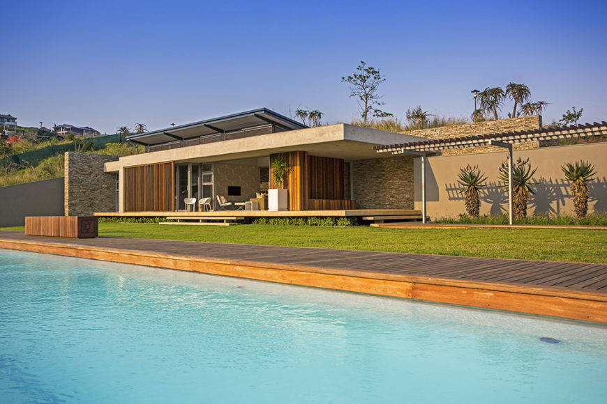 Over the cool waters of the pool, we see how the rich wood deck mimics the look of the wood found wrapped around the home itself, appearing on the deck, feature walls, and louvers.
