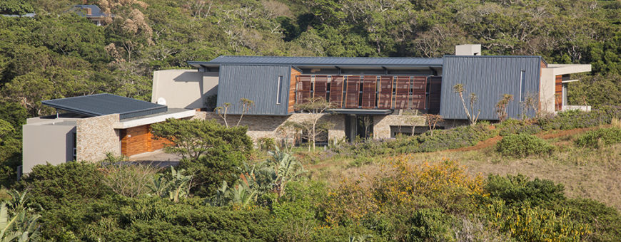 From a distance, we can see the intricate layering of the home's construction, with an angled steel roof raised above the stone and natural wood structure.