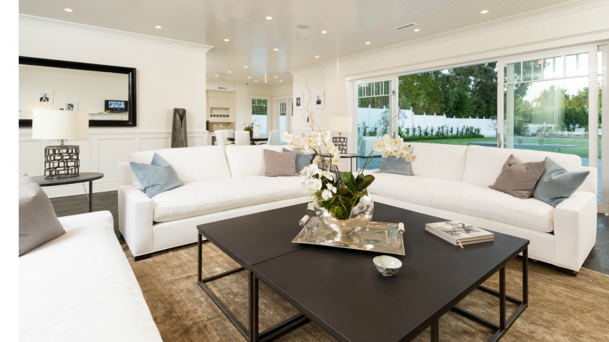 This living room designed with neat and clean white walls, and the ceiling literally gleams as natural light passes through an open glass entrance. The wood flooring is a good counterpart to the wooden center table.