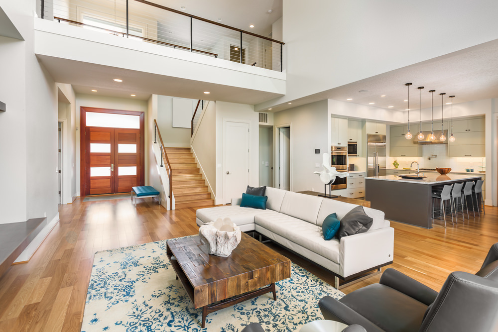 An open concept space with a living area next to the kitchen and dining area. The mixture of brown, grey, blue and white is quite pleasing and inviting. This exemplifies a contemporary minimalist design with a few added decorations.
