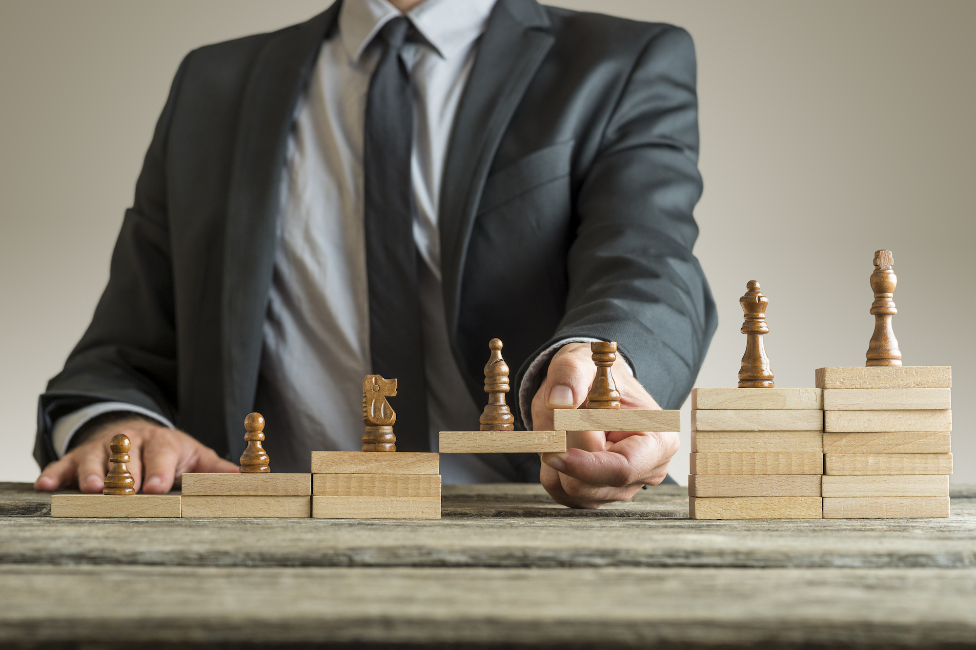Conceptual image of career management Conceptual image of career management with a businessman forming a bridge of wooden building blocks for chess pieces developing from pawn to king.