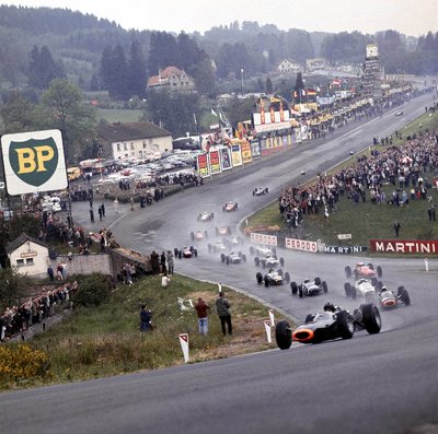1965 Belgian Grand Prix. Spa-Francorchamps, Belgium. 11-13 June 1965. Graham Hill leads Jackie Stewart (Both BRM P261's), Richie Ginther (Honda RA272), Jo Siffert (Brabham BT11 BRM), John Surtees (Ferrari 158), Dan Gurney (Brabham BT11 Climax) and the rest of the field through Eau Rouge at the start. by Anonymous - print