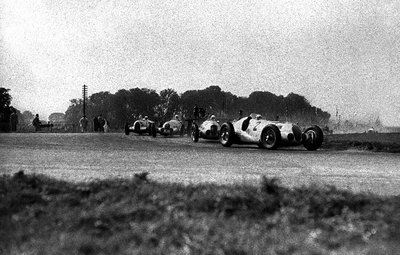 1937 Donington Grand Prix. Donington Park, Great Britain. 2 October 1937. Hermann Lang leads Rudolf Caracciola, Dick Seaman (all Mercedes-Benz W125) and Bernd Rosemeyer (Auto Union C-typ). Rosemeyer, von Brauchitsch and Caracciola finished in 1st, 2nd and 3rd positions respectively. by Anonymous - print