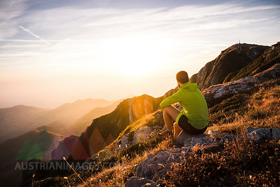 Italy, mountain running man sitting on rock looking at sunset