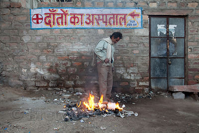 In a ritual repeated across India every morning, a man warms himself by a pile of burning garbage, Jodhpur, Rajasthan, India