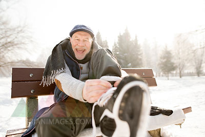 Portrait of happy senior man sitting on bench in winter landscape putting on ice skates