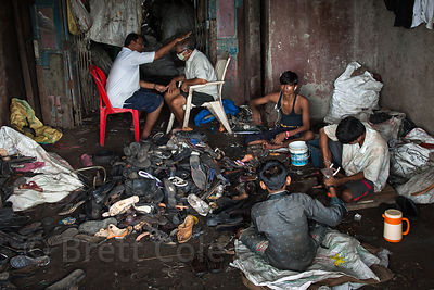 The much lauded recycling program in the Dharavi slum in Mumbai, India is not all positives. Here children work in a dark, dirty, poorly ventilated room dismantling old shoes and sandals, while their taskmaster sits in a chair all day wearing a face mask to guard against the rubber particles and the constant exhaust fumes from the busy road outside the shop. Here he is receiving a blessing. The bulk of the recycling in Dharavi is plastic, and children work in many of those shops as well.