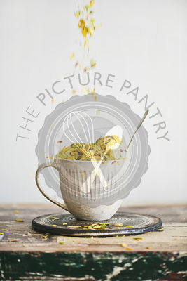Pistachio ice cream in mug with nuts falling from above