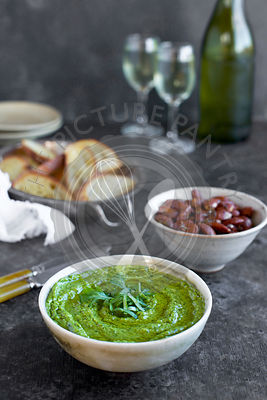 Arugula Chive Basil Pesto served in a ceramic bowl with crostini, almonds and wine. Photographed fron front view on a black/brown background.