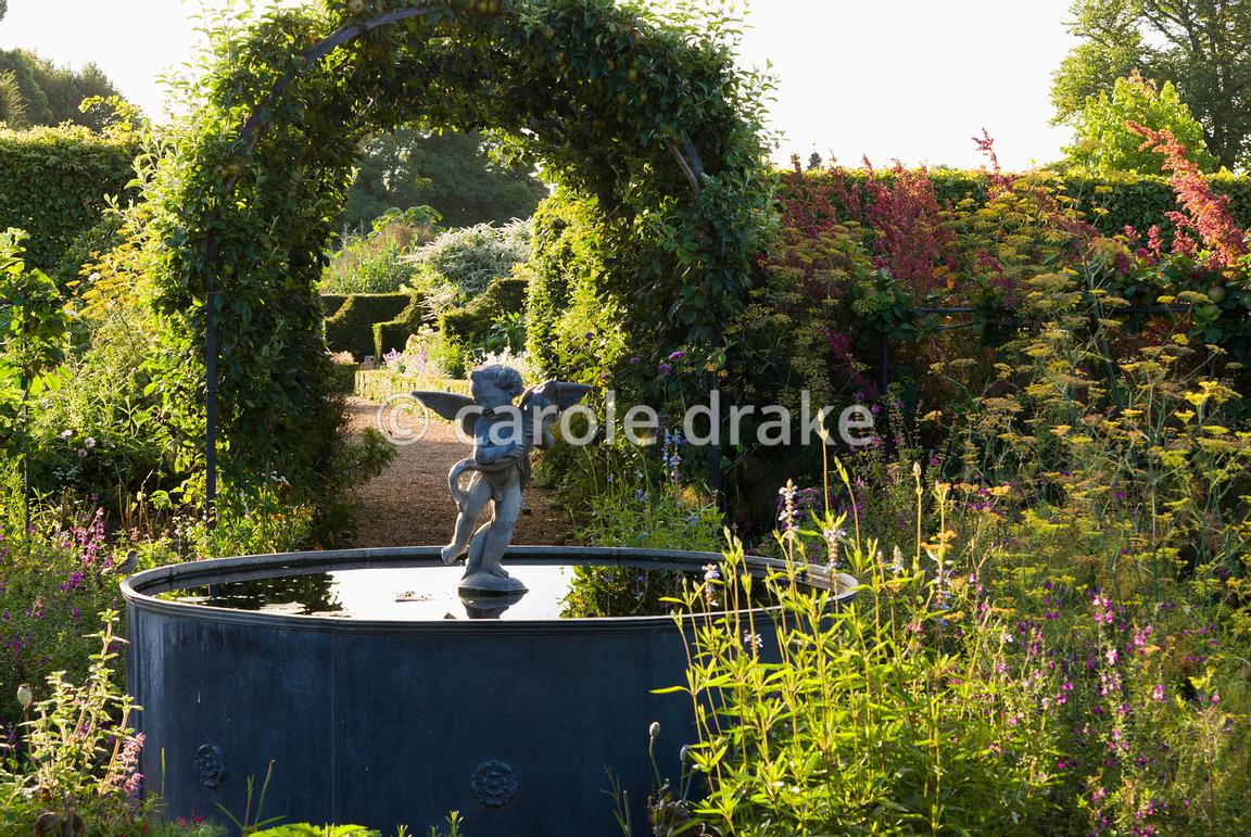 Lead fountain with putto and dolphin at the centre of the Organic Kitchen and Flower Garden, with apple tunnels shading the nearby paths. Arundel Castle Gardens, Arundel, West Sussex, UK
