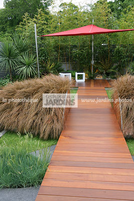 Jardin contemporain. Dallage bois. Passage surélevé. Carex comans 'Milk Chocolate'. Coin repos. Voile d'ombrage. Parasol. Irlande. Paysagistes : Com Doyle et Dean Lacey