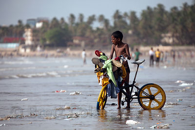 A boy rides his bike along a trash-strewn stretch of Juhu Beach, Mumbai, India.