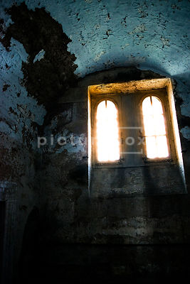 Dirty windows letting light into a damp and decaying prison cell.