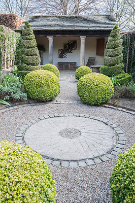 The Herb Garden with topiary box and yew shapes, a summerhouse at one end, and a central gravel path edged with stone setts. York Gate Garden, Adel, Leeds, Yorkshire