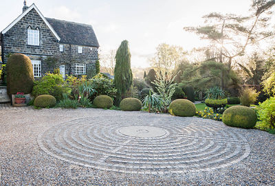Pavement maze created with stone setts in gravel in the driveway, surrounded by clipped yew spheres and other shrubs. York Gate Garden, Adel, Leeds, Yorkshire