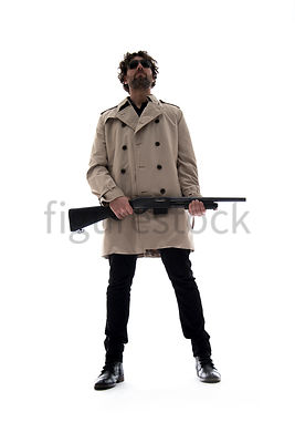 A Figurestock image of a man in a mac, standing, holding a shotgun – shot from low level.