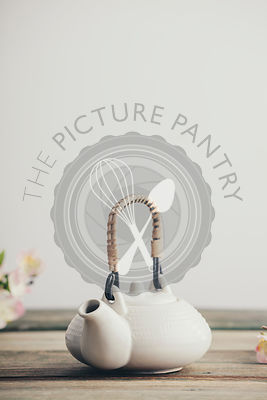 White teapot and sakura flowers on wooden table against the white wall