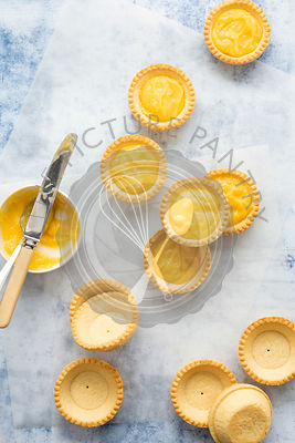Empty and filled lemon tartlets with a bowl of lemon curd and a knife.