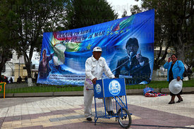 Ice cream seller below banner with president Evo Morales Ayma and Eduardo Avaroa , Plaza Avaroa , La Paz , Bolivia