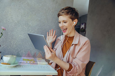 Woman with tablet waving to somebody during a video conference in a cafe