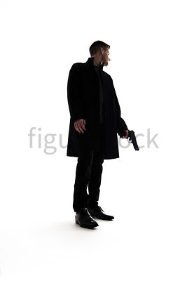 A Figurestock image of a mystery man standing, holding a gun, in silhouette – shot from low level.