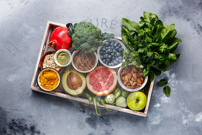 Healthy food clean eating selection in wooden box: fruit, vegetable, seeds, superfood, cereals, leaf vegetable on gray concrete background