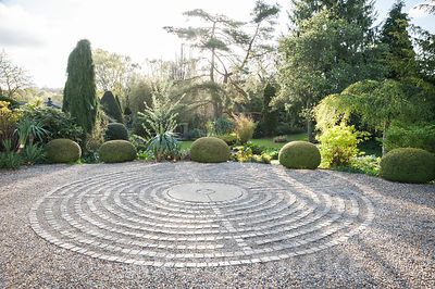 Pavement maze created with stone setts in gravel in the driveway, surrounded by clipped yew spheres and other shrubs. York Gate Garden, Adel, Leeds, Yorkshire