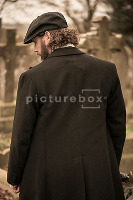 A vintage man in a peaky cap standing in a cemetery.