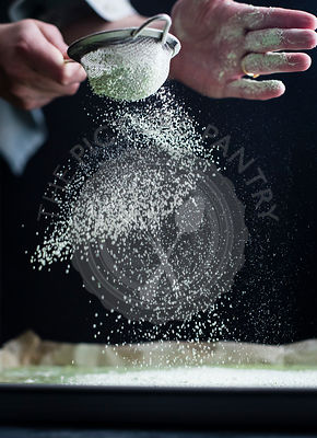A cooks hands sprinking matcha icing sugar on to a baking tray