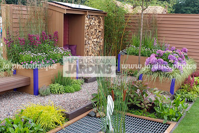 Abri de jardin dans un jardinet urbain. Jardinière en plastique recyclé. Carex elata 'Aurea', Geranium sanguineum, Hydrangea macrophylla 'Teller Blue', Grille en fer. Paysagiste : Tim Fowler, TPFS, Angleterre