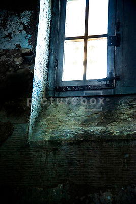 A dirty window letting light into a damp and decaying prison cell.