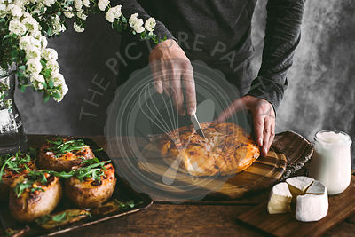 Man's hand cutting bread on wooden board. Preparation for lunch. Rustic backgraund
