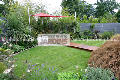 Jardin contemporain, jardinet. Pelouse. Coin repos. Voile d'ombrage. Cordyline australis. Irlande. Palissade en bois peint, claustra. Dallage en bois, terrasse. Paysagistes : Com Doyle et Dean Lacey
