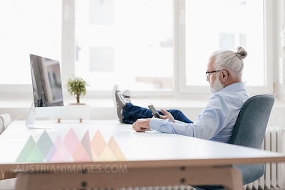 Mature man with beard using cell phone at desk