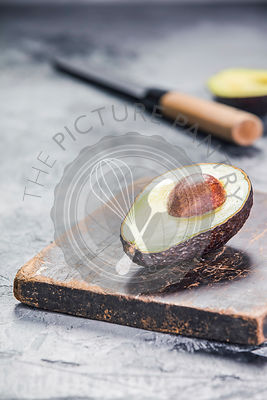 Green ripe avocado and knife on a grey stone background