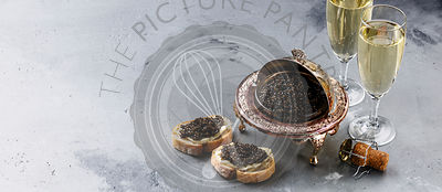 Black caviar in silver bowl, sandwiches and champagne on gray concrete background copy space