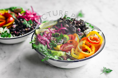 Vegan burrito bowls with spicy black beans, rice, summer vegetables, and pickled onons